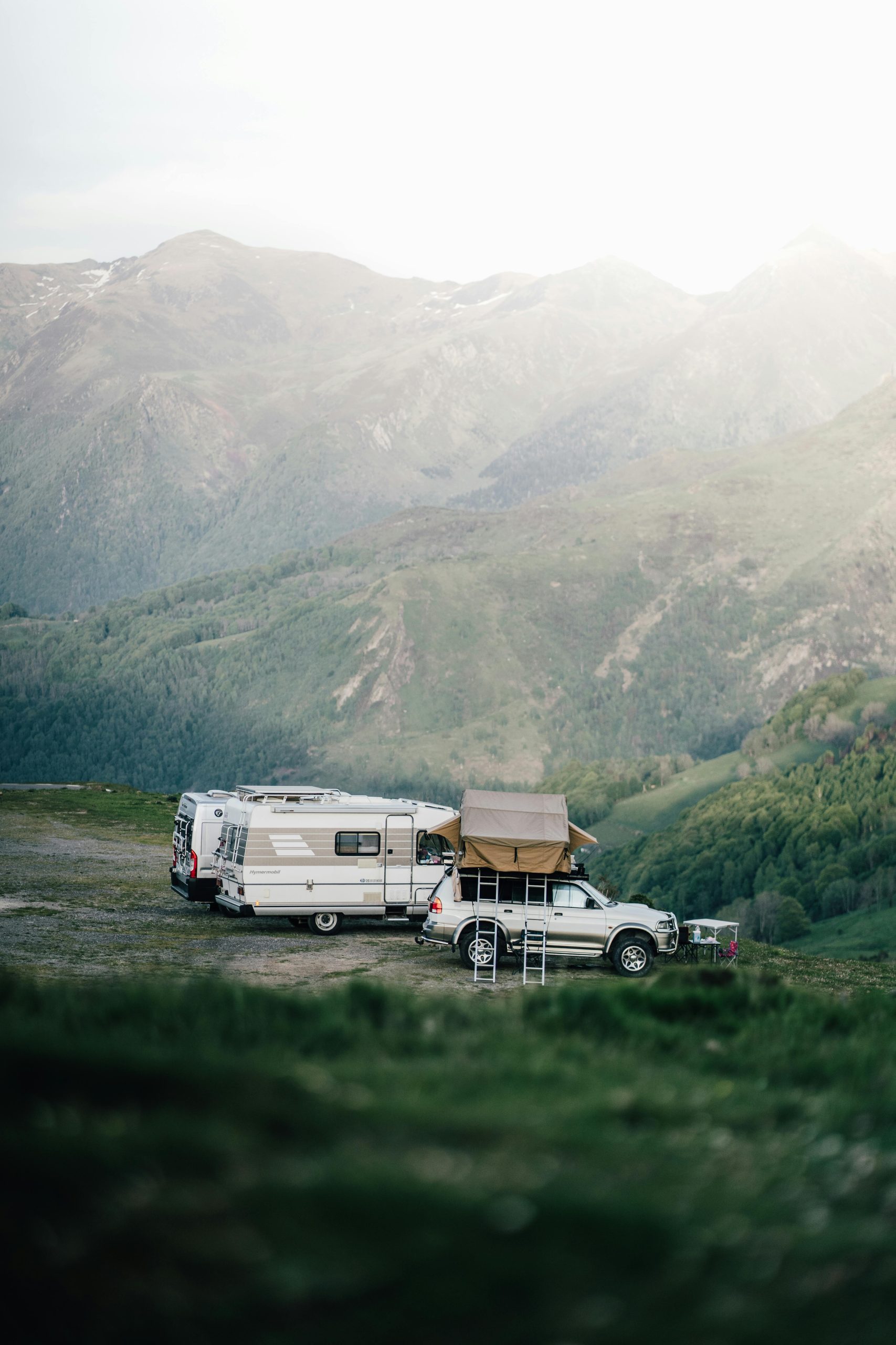 A car and camper van set up camp in a serene mountainous landscape, perfect for an adventurous escape.